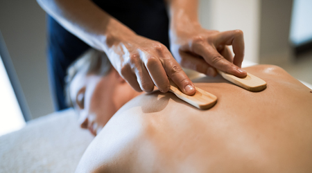 Massage therapist using wooden tool to massage patientの写真素材