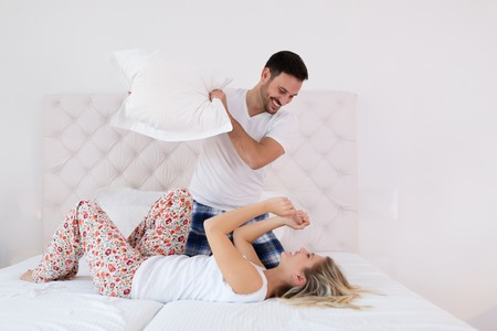 Happy couple fighting with pillows in bedの写真素材