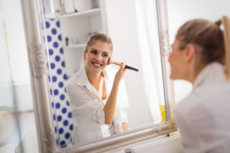 Beautiful girl in bathroom applying makeupの写真素材