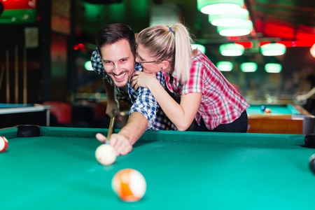Young couple playing together pool in bar