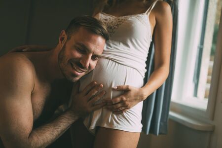 Happy pregnant woman enjoying with husband in bedroomの写真素材