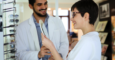 Woman choosing her new glasses at optics store with help of ophthalmologistの写真素材