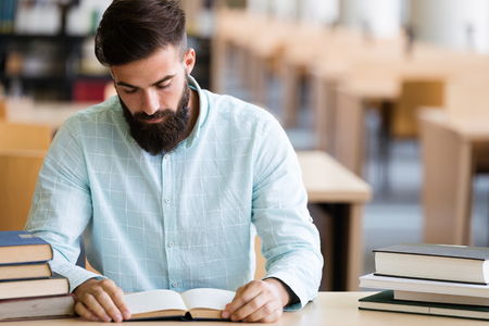 Serious male student reading book in the college libraryの写真素材