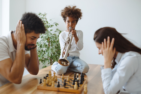 Mother and father trying to play chess while their child plays trumpetの写真素材