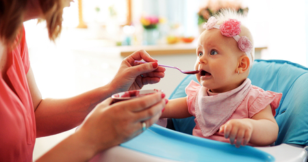 Mother feeding baby with spoon indoorsの写真素材