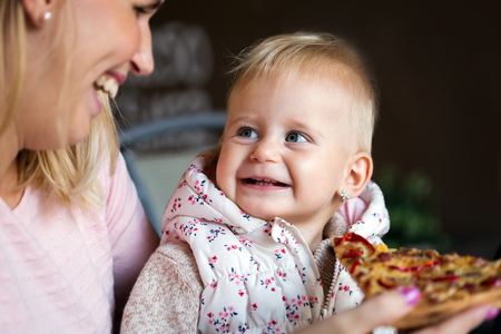 Little girl eats a large slice of pizza from her mothers hands. Childrens pizza.の写真素材