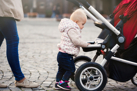 Beautiful toddler girl playing with his stroller walking outdoors