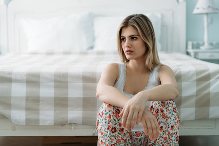 Depressed young woman sitting on bed at homeの写真素材