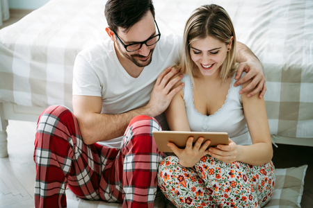 Young happy couple using tablet in bedroomの写真素材