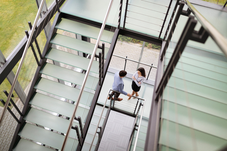 Modern business people walking on stairs in glass hall in office buildingの写真素材