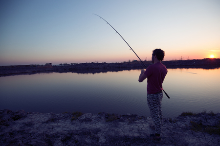 Young man fishing at pond and enjoying hobbyの写真素材