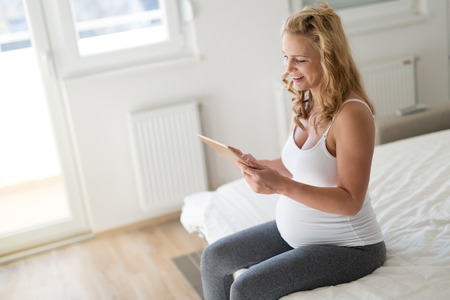 Happy pregnant woman using tablet in bedroom