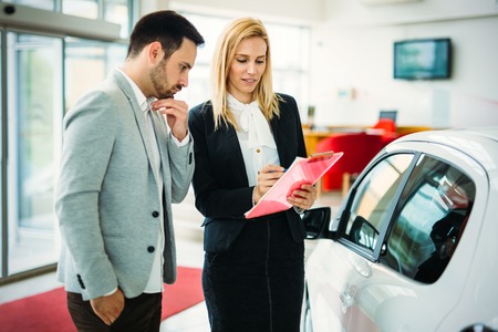 Young female car sales consultant working in showroomの写真素材
