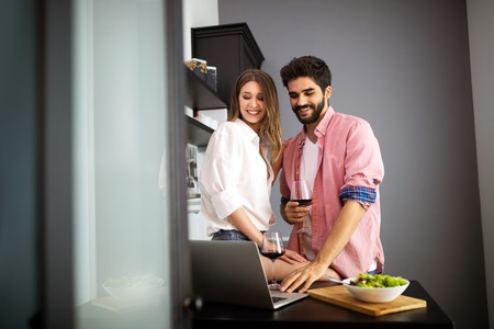 Happy couple using laptop while having breakfast in kitchenの写真素材