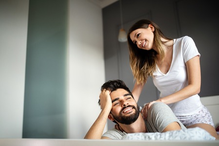 Young woman is doing her handsome boyfriend massage and smiling while they are resting at homeの写真素材