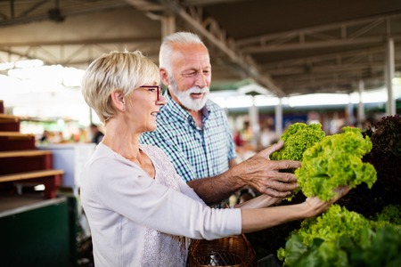 Senior family couple choosing bio food fruit and vegetable on the market during weekly shoppingの写真素材