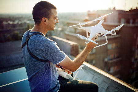 Young technician flying UAV drone with remote control on rooftop