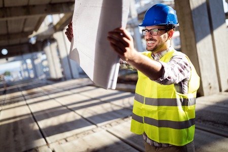 Engineer working on construction site and holding blueprint