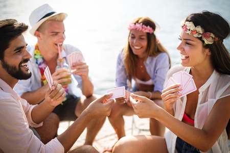 Group of young friends having fun while playing cards on beachの写真素材