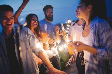 Happy friends with drinks toasting at rooftop party at night