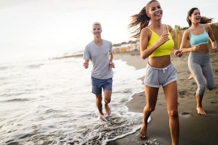 Group of friends running at the beach on beautiful summer sunsetの写真素材