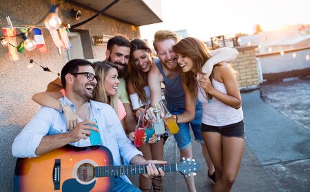Young friends having fun at a rooftop party, playing the guitar, singing, dancing and drinkingの写真素材