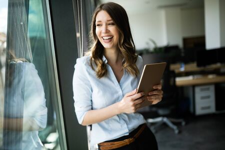 Happy woman manager holding tablet and standing in modern officeの写真素材