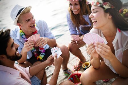 Group of young friends having fun while playing cards on beachの写真素材