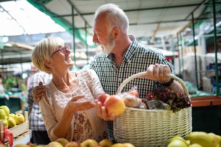Smiling senior couple holding basket with vegetables at the marketの写真素材