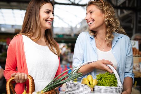 Young women friends baying vegetables and fruits on the marketの写真素材