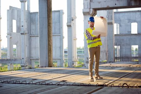 Engineer working on construction site and holding blueprint