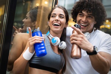 Young man and woman having break after running workout and drinking waterの写真素材