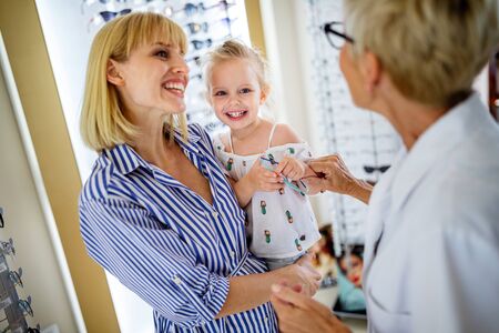 Optician helping to find a perfect glasses to little girl at optics storeの写真素材