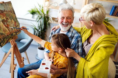 Happy grandparents and granddaughter drawing, painting togetherの写真素材