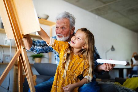 Senior man with child painting on canvas. Grandfather spending happy time with granddaughter.の写真素材