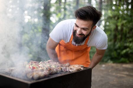 Handsome male preparing barbecue, grill outdoors for friendsの写真素材