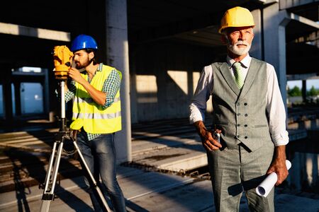 Two satisfied engineers talking at building site with construction structure in background
