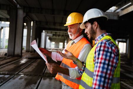 Two satisfied engineers talking at building site with construction structure in background