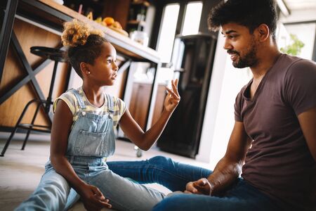 Cute african girl and her handsome father are talking and smiling at homeの写真素材