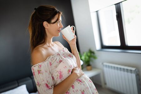 Young pregnant woman at home sipping tea from a cupの写真素材