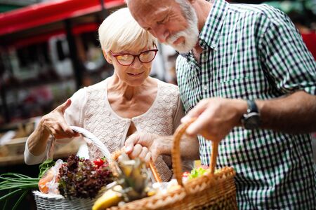 Smiling senior couple holding basket with vegetables at the marketの写真素材
