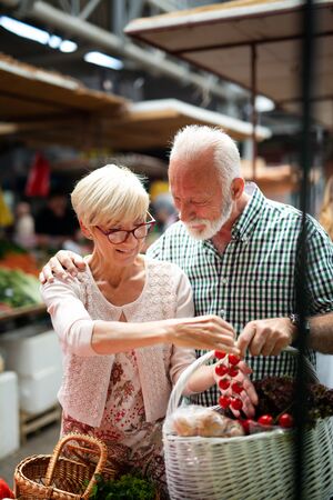 Smiling senior couple holding basket with vegetables at the grocery shopの写真素材