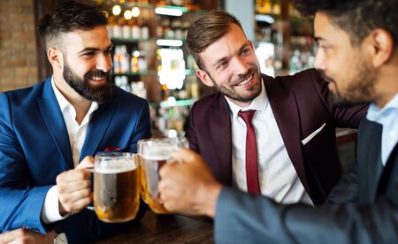 Handsome businessmen are drinking beer, talking and smiling while resting at the pubの写真素材