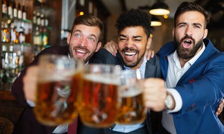 Men fans screaming and watching football on TV and drink beer in a pubの写真素材