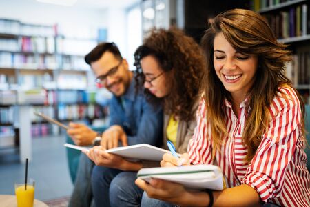 Group of happy students reading books and preparing to exam in libraryの写真素材
