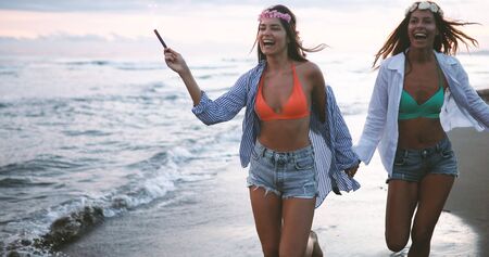 Happy group of friends lighting sparklers and enjoying freedom at beach during sunset