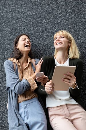 Smiling young lesbian girls having fun with tablet outdoorの写真素材