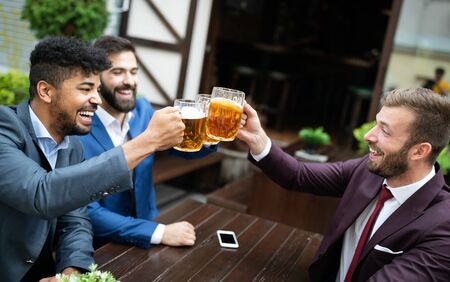 Meeting with the best friends. Happy young business men talking and drinking beer in a pubの写真素材