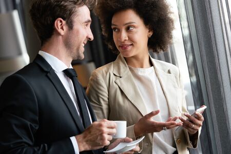 Portrait of businessman drinking coffee, talking to woman colleagueの写真素材