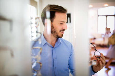 Handsome man choosing glasses in optics store.